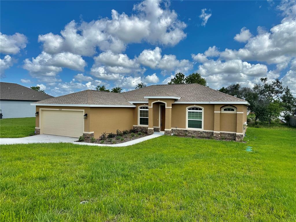A single-story house with a tan stucco exterior, stone accents, and a two-car garage — 13075 HOUSE FINCH ROAD, WEEKI WACHEE, FL
