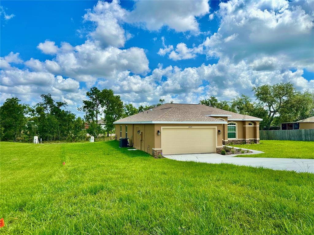 A tan single-story house with a two-car garage sits on a large, grassy lot — 13075 HOUSE FINCH ROAD, WEEKI WACHEE, FL