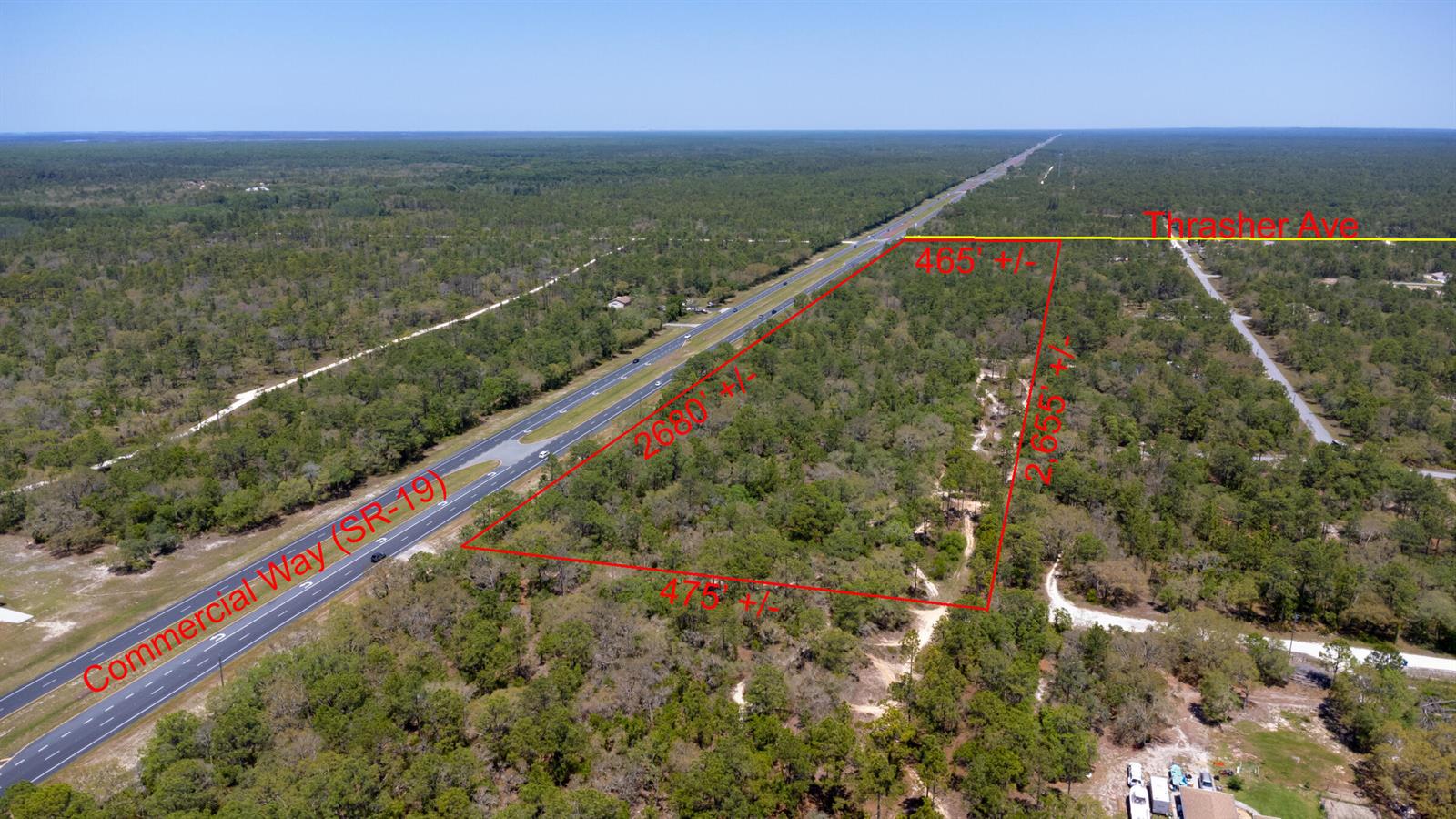 An aerial view shows a large, wooded plot of land bordering a highway and road — 0 Thrasher Avenue, FL 34614, FL