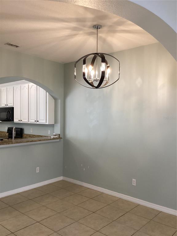A dining area with tile floors, a modern orb chandelier, and an arched kitchen opening — 11932 DEER PATH WAY, ORLANDO, FL