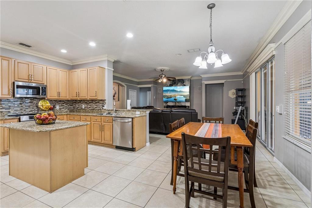 An open-concept kitchen and dining area features light wood cabinets, granite countertops, and tile flooring — 480 ROB ROY DRIVE, CLERMONT, FL