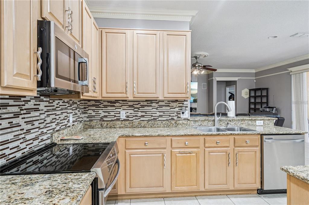 A kitchen featuring light wood cabinets, granite countertops, a stainless steel microwave, and tiled backsplash — 480 ROB ROY DRIVE, CLERMONT, FL