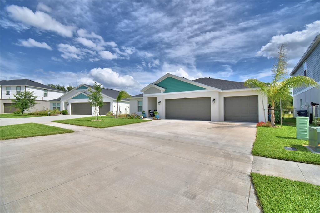 A single-story house with a three-car garage and teal accents under a cloudy sky — 1018 BRIMSTONE CIRCLE, WINTER HAVEN, FL