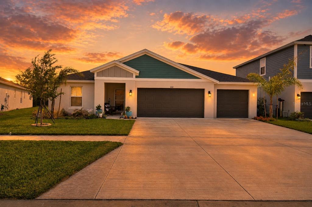 A single-story suburban house with a three-car garage and a concrete driveway at sunset — 1018 BRIMSTONE CIRCLE, WINTER HAVEN, FL