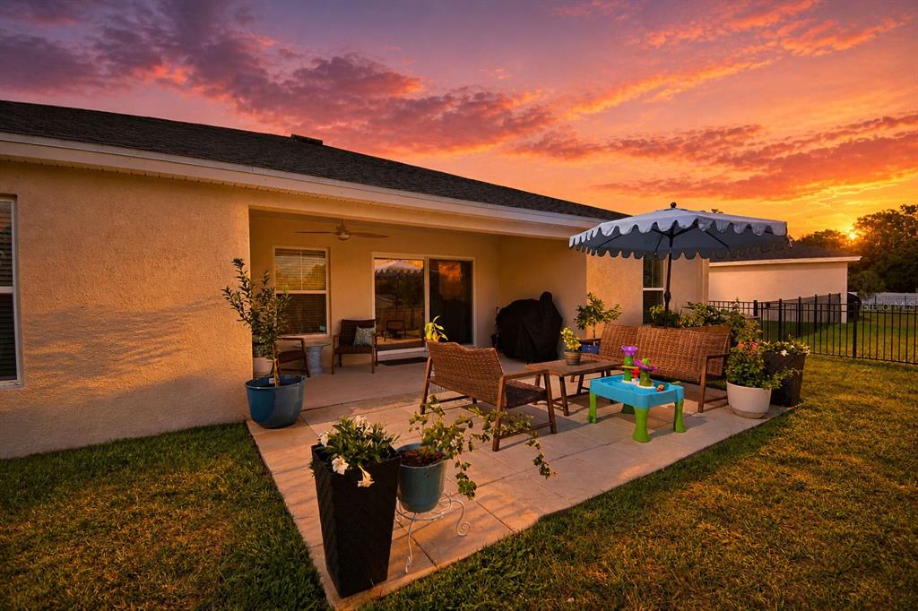 A patio with wicker furniture and an umbrella sits behind a house at sunset — 1018 BRIMSTONE CIRCLE, WINTER HAVEN, FL