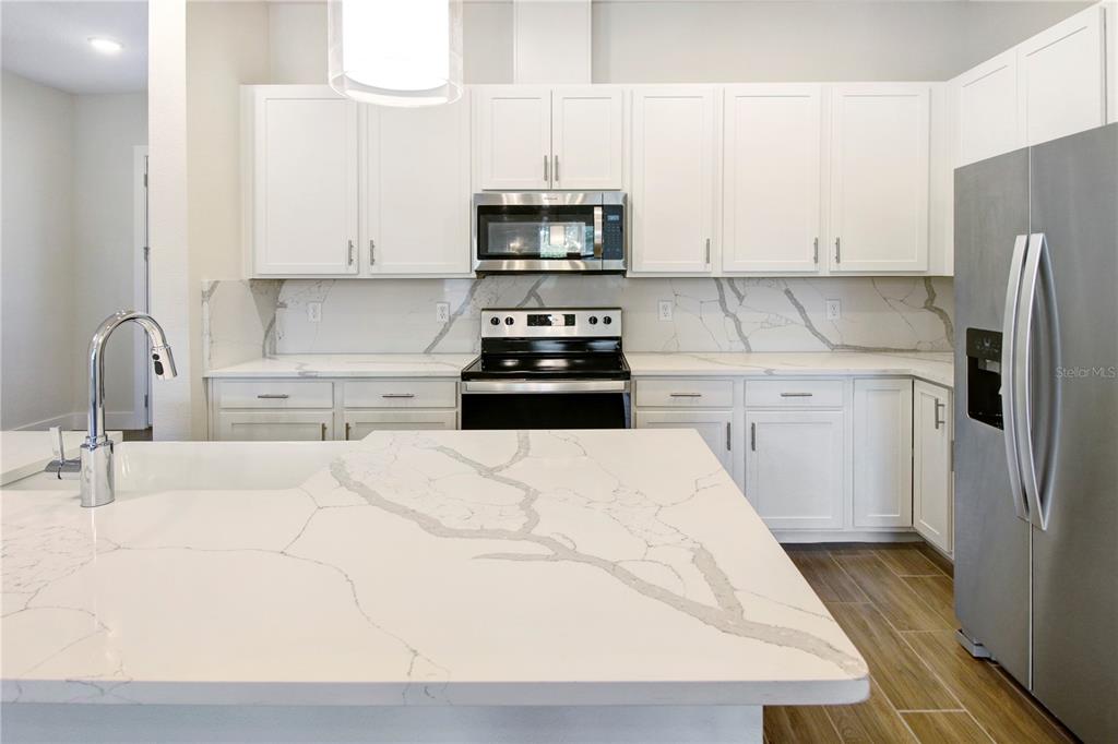A modern kitchen features white cabinets, stainless steel appliances, and a marble-patterned quartz island — 1604 BIRCHFIELD COVE, OVIEDO, FL