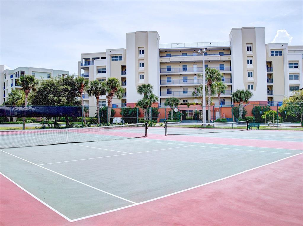 A tennis court sits in front of a multi-story apartment building with palm trees — 5300 S ATLANTIC AVENUE UNIT 4-503, NEW SMYRNA BEACH, FL