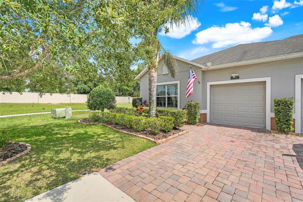 A single-story house exterior features a brick paver driveway, a garage, and landscaped front yard — 3550 FAIRWATERS COURT UNIT D, CLERMONT, FL