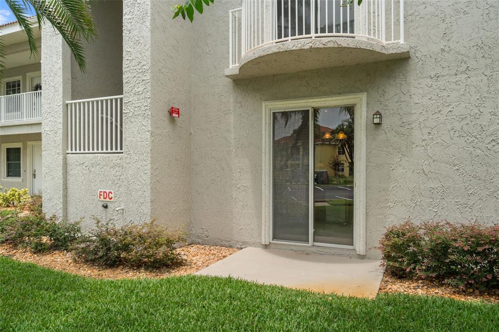 A ground-level apartment patio features a sliding glass door, a small concrete slab, and landscaping — 6808 DALI AVENUE UNIT 101, LAND O LAKES, FL