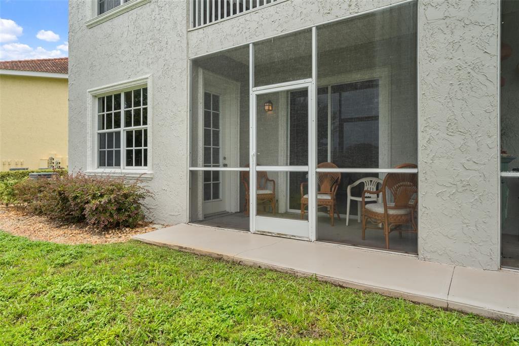 A screened-in patio with wicker chairs sits adjacent to a white stucco house exterior — 6808 DALI AVENUE UNIT 101, LAND O LAKES, FL