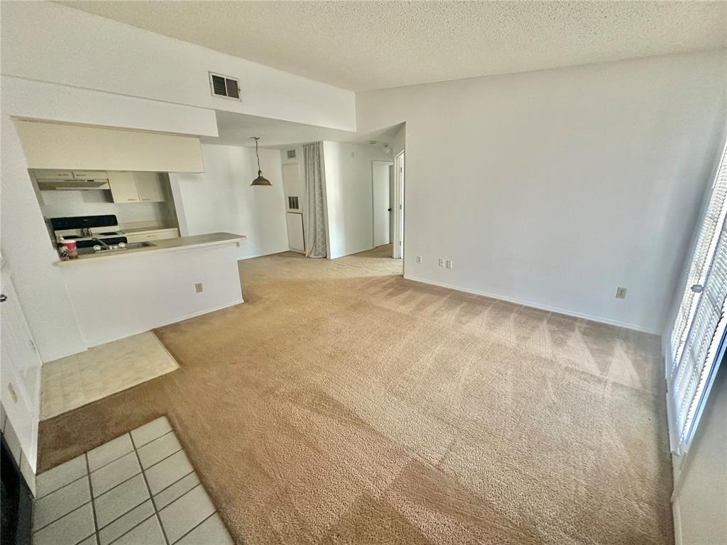 A living room with beige carpet, white walls, and an adjacent kitchen with a breakfast bar — 2550 N ALAFAYA TRAIL UNIT 3304, ORLANDO, FL