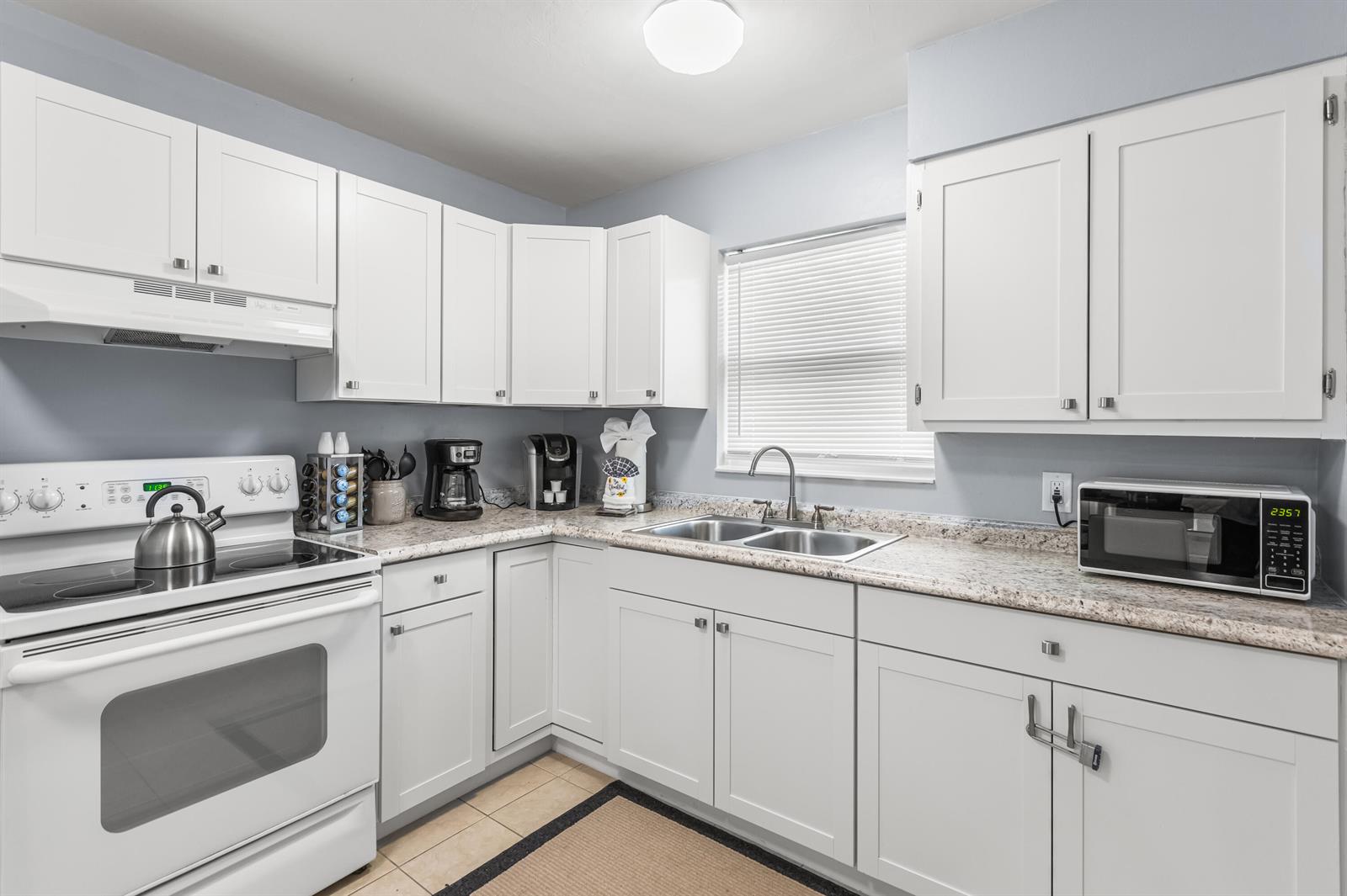 A kitchen with white cabinets, light-colored countertops, a white stove, and a stainless steel sink — 4953 Bayshore Drive, Naples FL 34112, NAPLES, FL