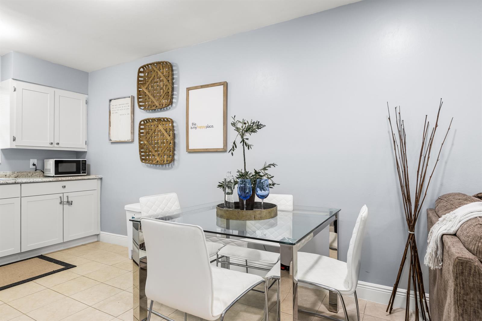 A dining area features a glass table, four white chairs, and wall-mounted basket decor — 4953 Bayshore Drive, Naples FL 34112, NAPLES, FL