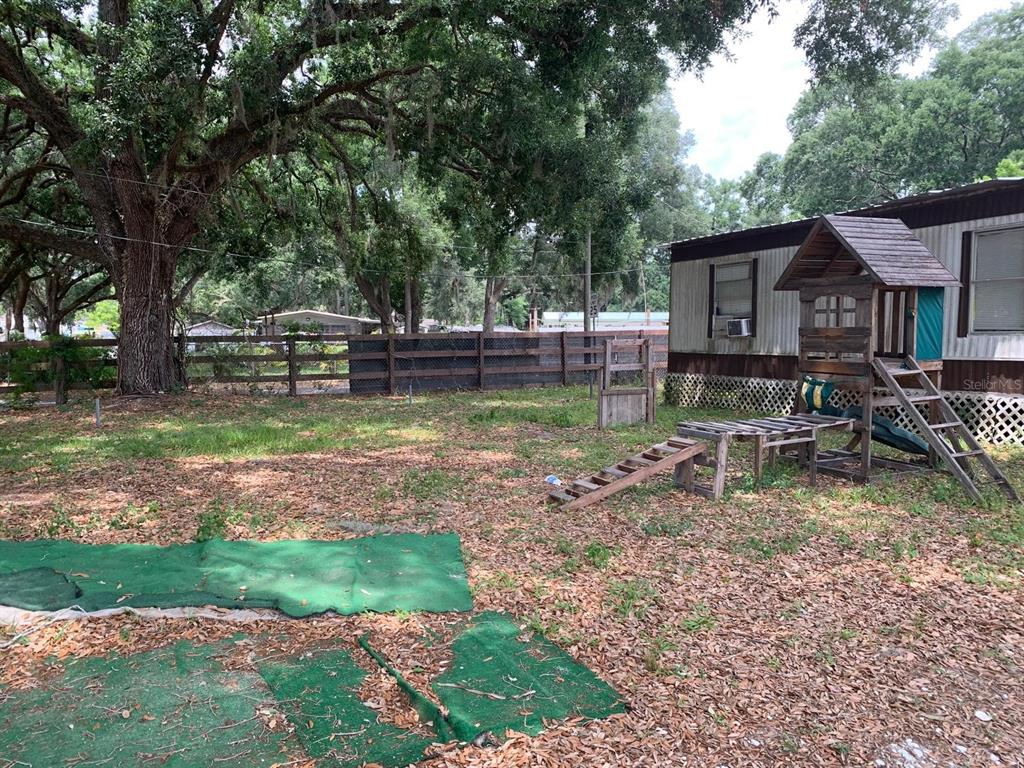 A backyard features a wooden playset, a mobile home, and a large oak tree — 11811 HAZEN AVENUE, THONOTOSASSA, FL