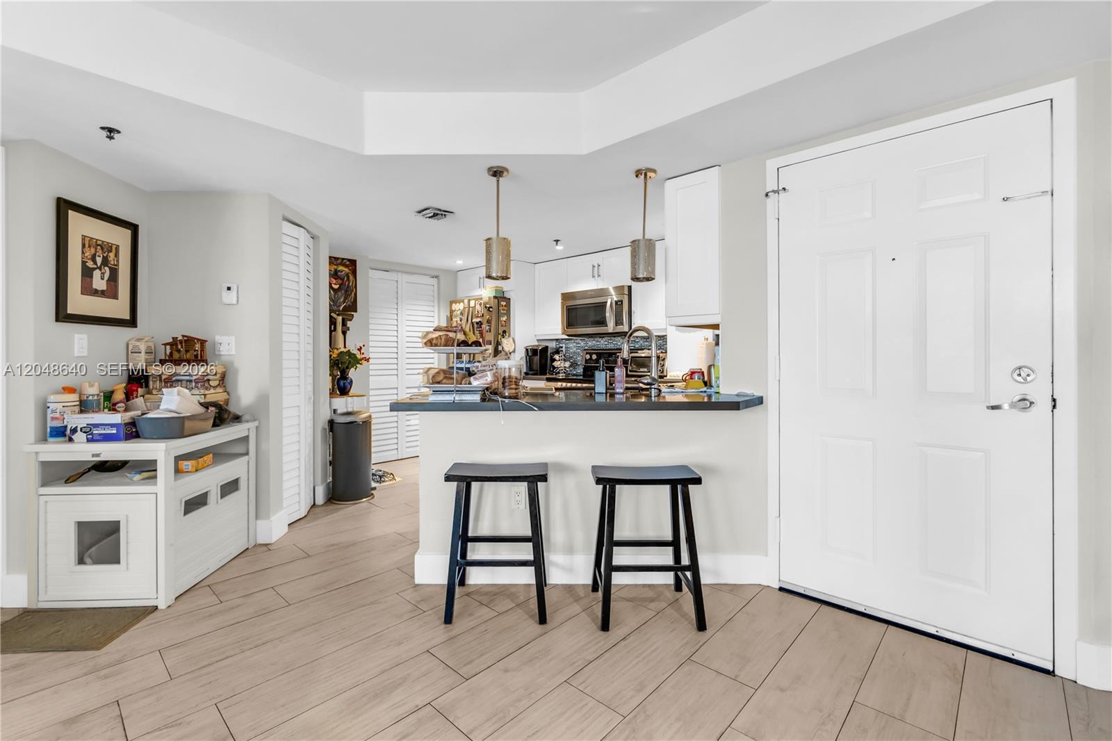A kitchen features a breakfast bar with two stools, white cabinetry, and light wood-look flooring — 2351 Douglas Rd # 1101, Miami FL 33145, MIAMI, FL