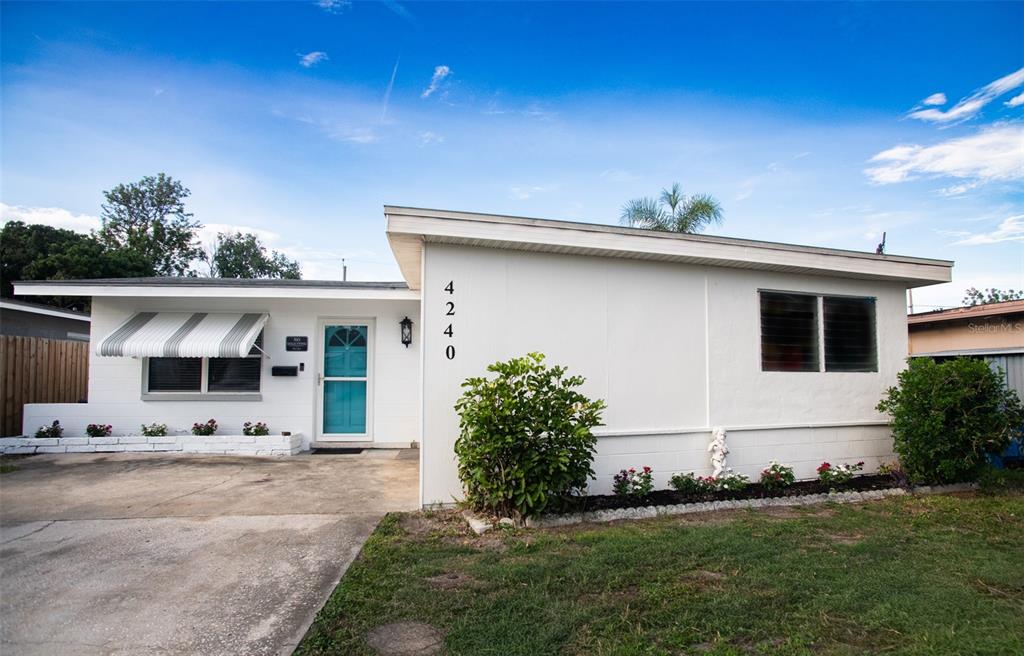 A single-story white house with a turquoise front door and a striped window awning — 4240 69TH AVENUE N, PINELLAS PARK, FL