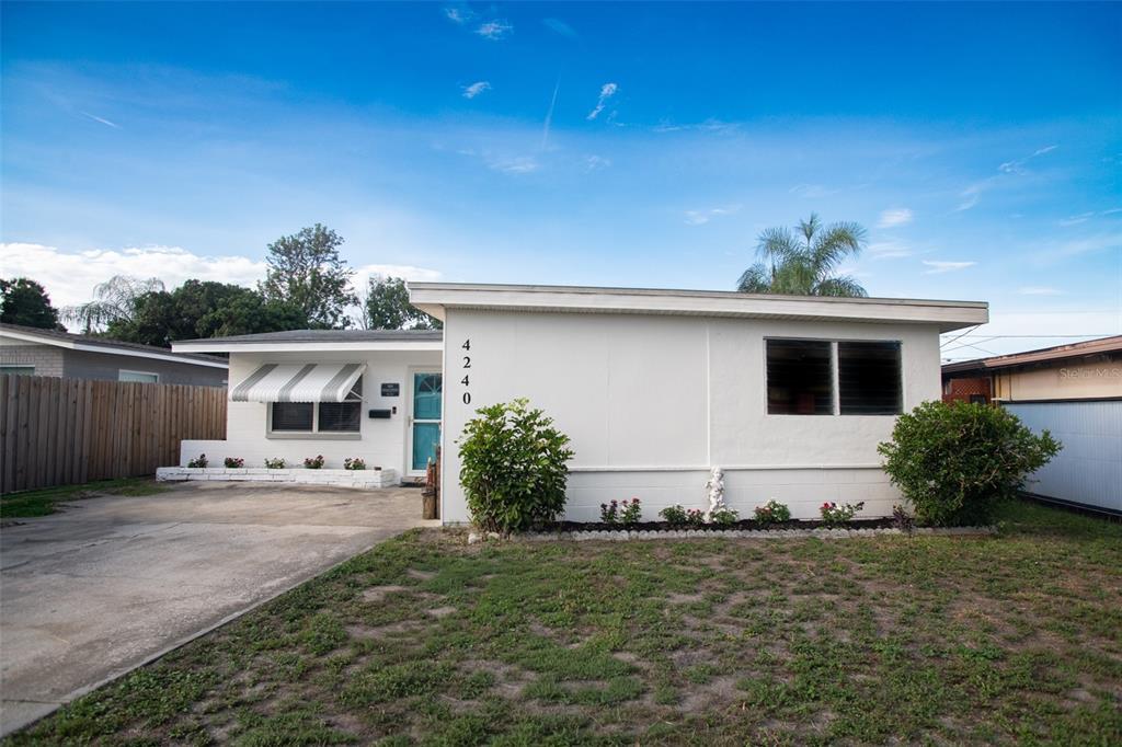 A single-story white house with a flat roof, a driveway, and a small front yard — 4240 69TH AVENUE N, PINELLAS PARK, FL