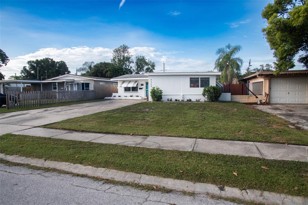 A white single-story house with a front lawn, concrete driveway, and sidewalk under blue skies — 4240 69TH AVENUE N, PINELLAS PARK, FL
