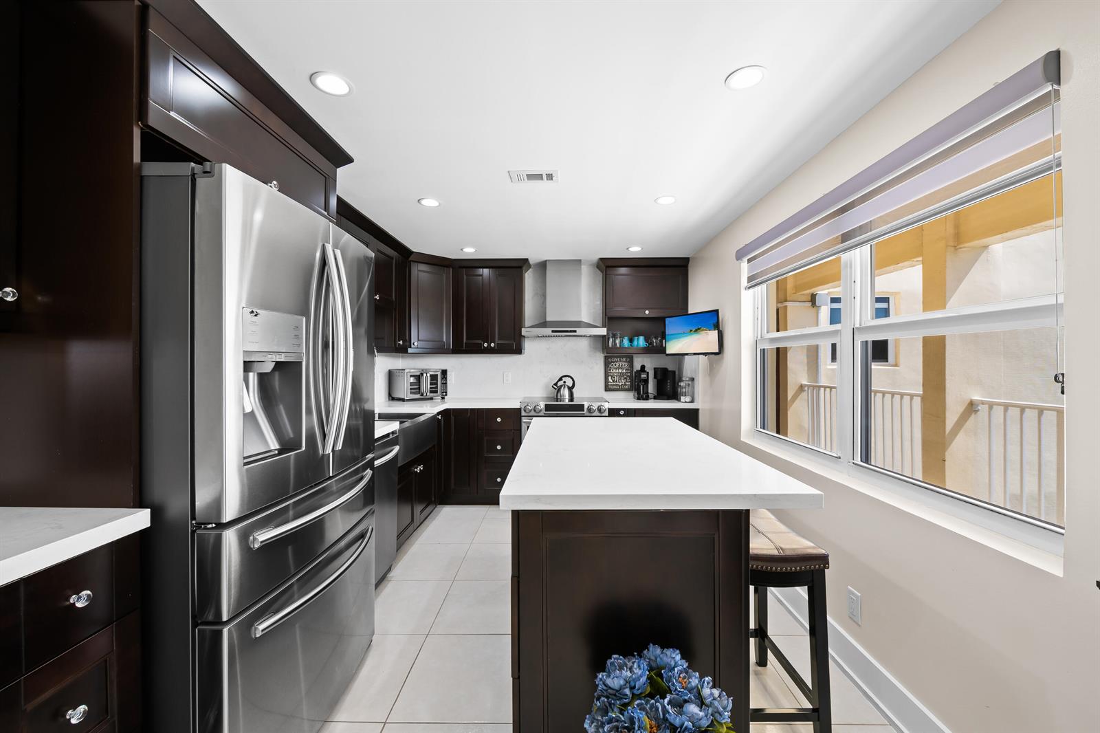 A kitchen features dark wood cabinetry, stainless steel appliances, a white island, and tile flooring — 3095 N Course Drive # 702, Pompano Beach FL 33069, POMPANO BEACH, FL