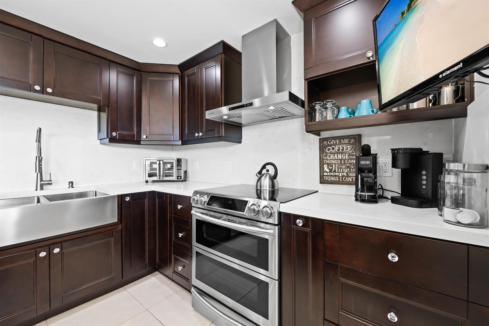 A kitchen features dark wood cabinets, stainless steel appliances, a farmhouse sink, and white countertops — 3095 N Course Drive # 702, Pompano Beach FL 33069, POMPANO BEACH, FL