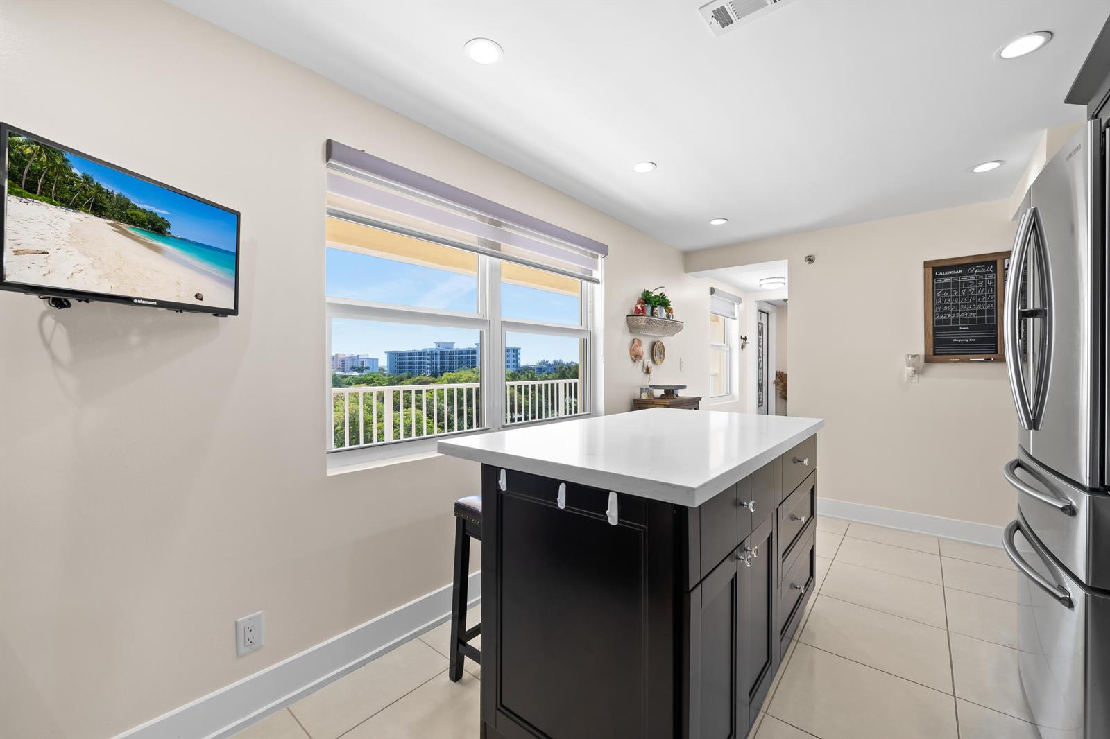 A kitchen features a dark island with a white countertop, a window, and a television — 3095 N Course Drive # 702, Pompano Beach FL 33069, POMPANO BEACH, FL