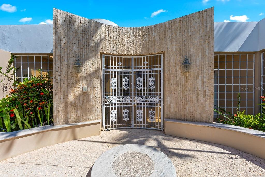 A curved stone wall features a white metal security gate leading to a home entrance — URB. SANTA MARIA 1906 CLL ORQUIDEA, SAN JUAN, PR