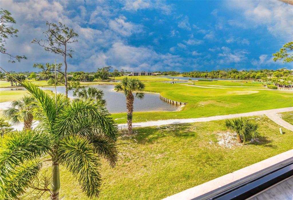 An elevated view of a golf course with a pond, palm trees, and green fairways — 24351 BALTIC AVE UNIT 203, PUNTA GORDA, FL