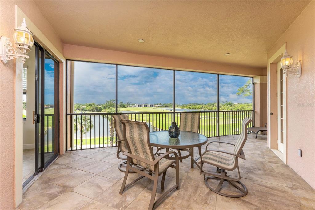 A screened-in patio features tile flooring, a glass-top table with chairs, and a golf course view — 24351 BALTIC AVE UNIT 203, PUNTA GORDA, FL