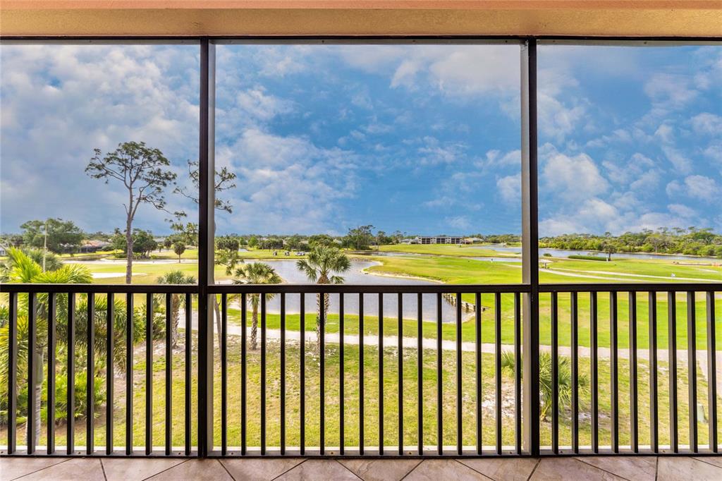 A screened-in balcony overlooks a golf course with a pond and scattered palm trees — 24351 BALTIC AVE UNIT 203, PUNTA GORDA, FL