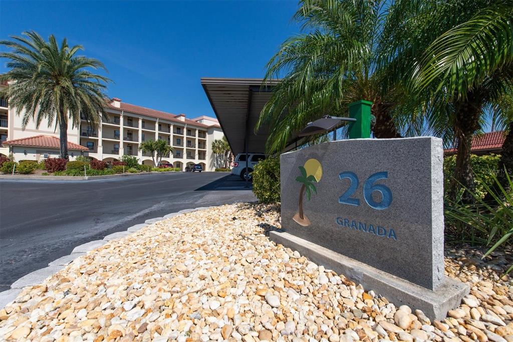A stone sign labeled 26 Granada stands in front of a multi-story apartment building — 19029 US HIGHWAY 19 N UNIT 26-208, CLEARWATER, FL