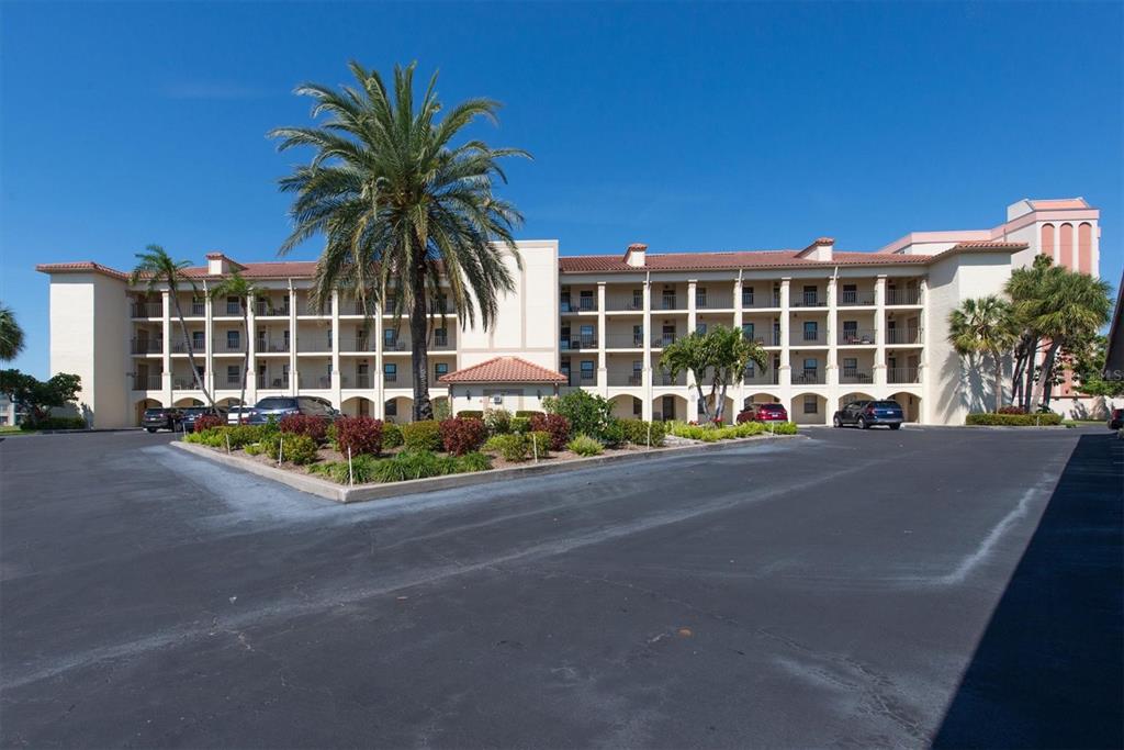A multi-story beige apartment building features open balconies, a tiled roof, and palm trees — 19029 US HIGHWAY 19 N UNIT 26-208, CLEARWATER, FL