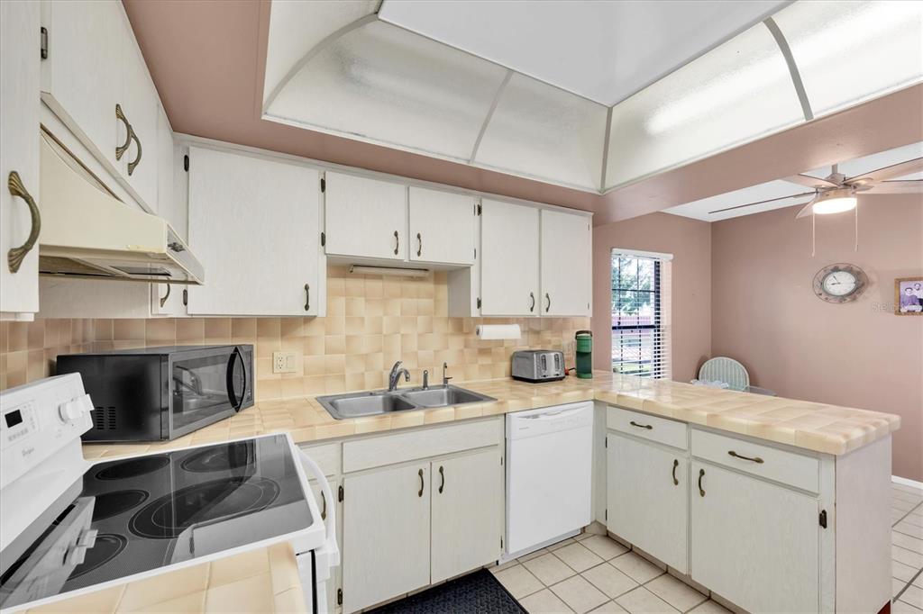 A kitchen features white cabinets, tiled countertops, a double sink, and a white appliance suite — 19029 US HIGHWAY 19 N UNIT 26-208, CLEARWATER, FL
