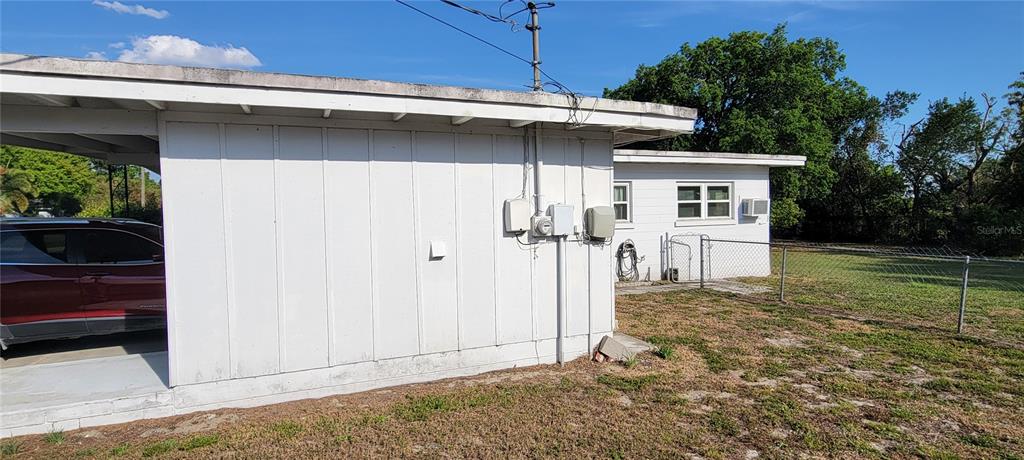 The exterior of a white house features a carport, utility meters, and a chain-link fence — 1540 AVENUE C NE, WINTER HAVEN, FL