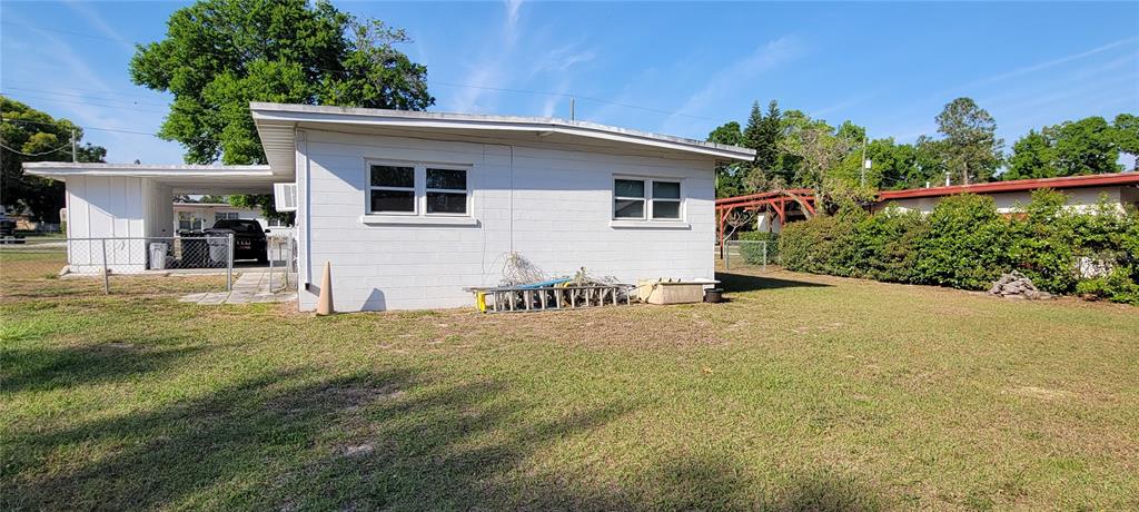 The exterior of a white concrete block house features a carport and a grassy yard — 1540 AVENUE C NE, WINTER HAVEN, FL