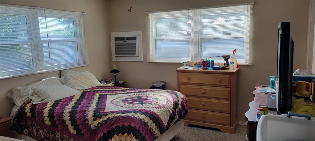 A bedroom features a bed with a patterned quilt, a wooden dresser, and window blinds — 1540 AVENUE C NE, WINTER HAVEN, FL