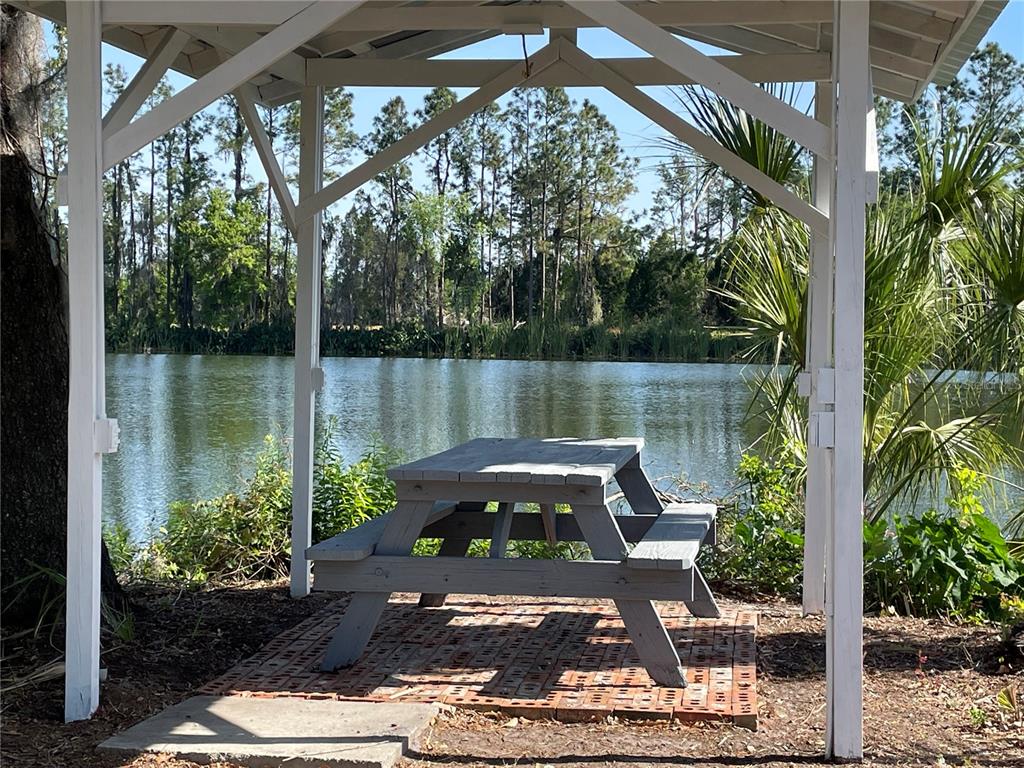 A covered stone patio features rocking chairs, ceiling fans, and a view of a lake — 701 E 60 HIGHWAY, PLANT CITY, FL