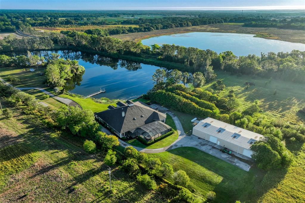 A large, single-story house with a hip roof and dormers sits beside a grassy pond — 701 E 60 HIGHWAY, PLANT CITY, FL