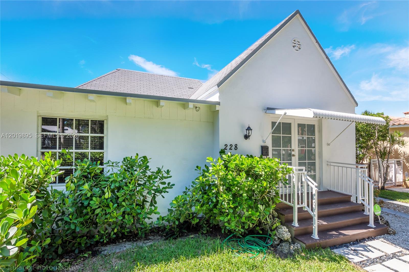 A white stucco house features a gray shingled roof, a front porch, and green landscaping — 228 SW 23rd Rd, Miami FL 33129, MIAMI, FL