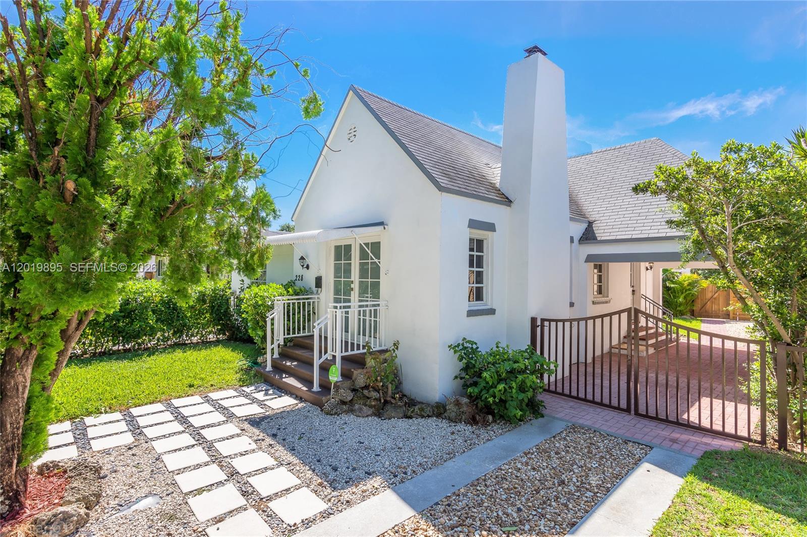 A white cottage with a steep roof, a tall chimney, and a gated brick driveway — 228 SW 23rd Rd, Miami FL 33129, MIAMI, FL