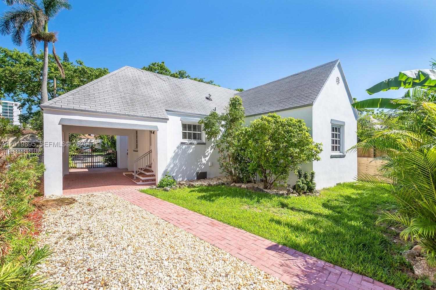 A white single-story house features a brick driveway, a covered carport, and a grassy lawn — 228 SW 23rd Rd, Miami FL 33129, MIAMI, FL