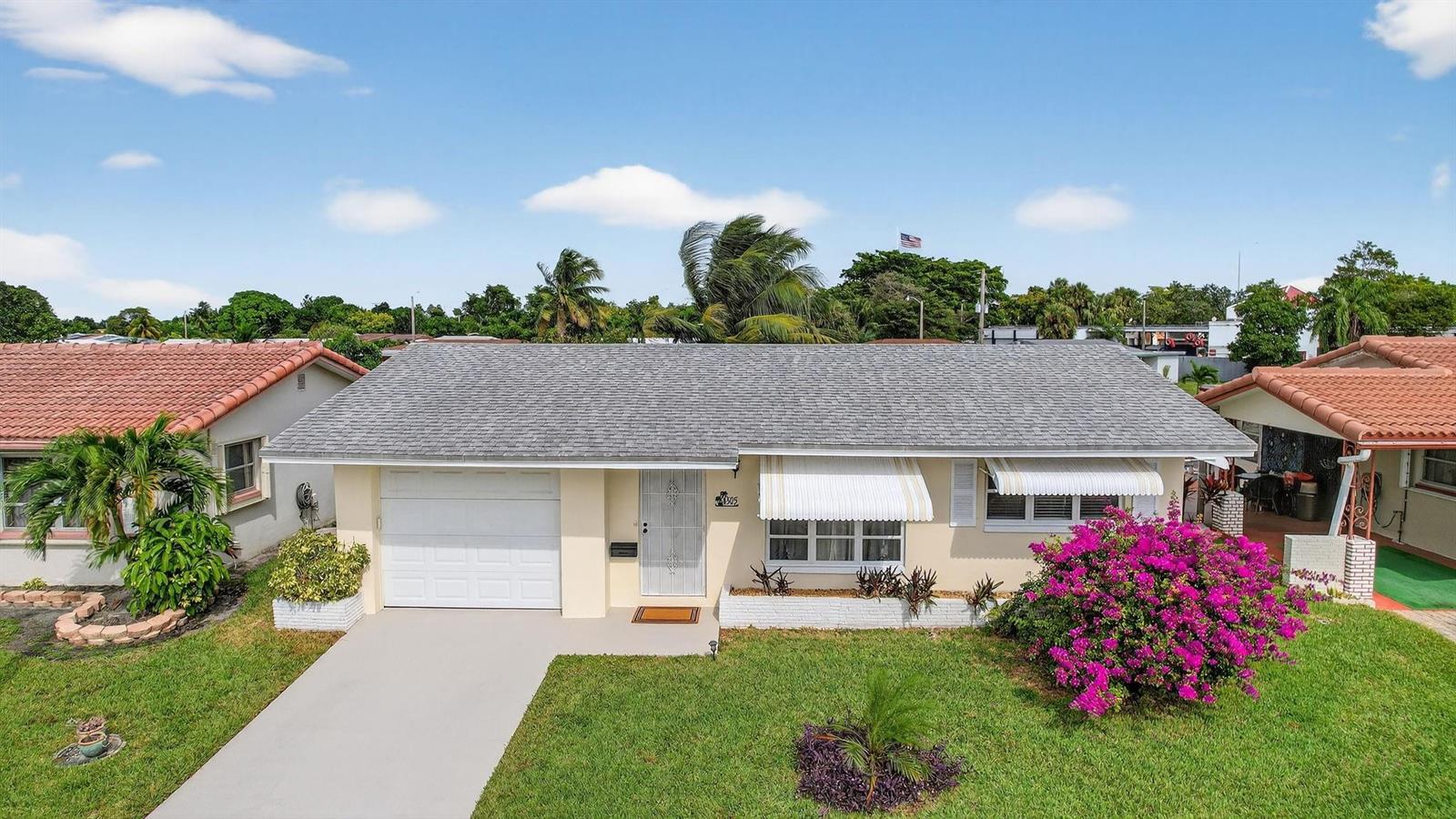 A single-story house with a white garage, gray roof, and a vibrant pink bougainvillea bush — 4305 NW 49th Drive, Tamarac FL 33319, TAMARAC, FL