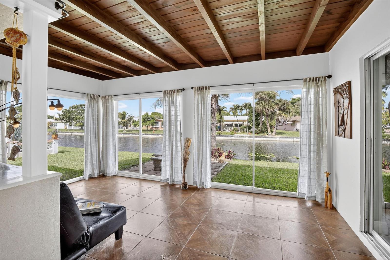 A sunroom with a wood-beamed ceiling, tile floors, and sliding glass doors overlooking a canal — 4305 NW 49th Drive, Tamarac FL 33319, TAMARAC, FL