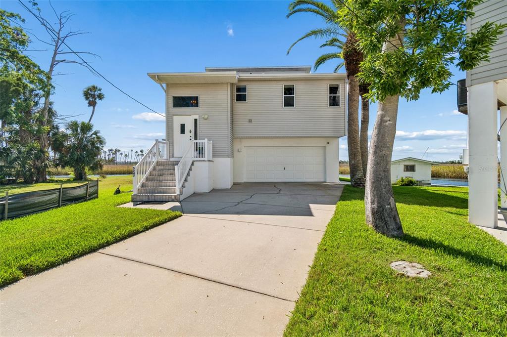 A two-story house with light siding, a white garage door, and an elevated front entrance — 5247 TROPICAL POINT, WEEKI WACHEE, FL