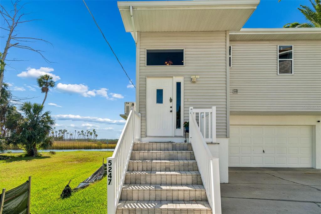 The exterior of a two-story house features a white front door, stairs, and a garage — 5247 TROPICAL POINT, WEEKI WACHEE, FL