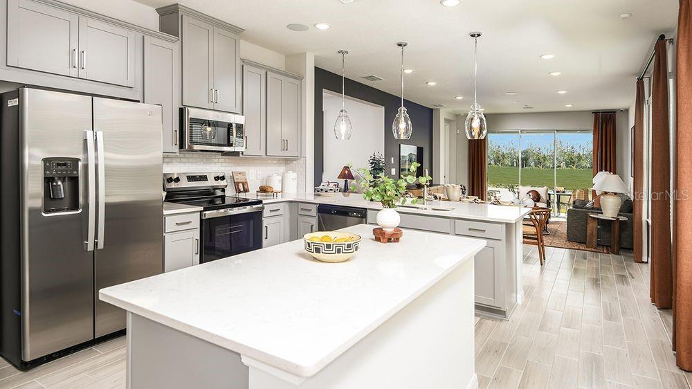 A modern kitchen features gray cabinets, stainless steel appliances, and a white quartz island — 32488 SEA LOCH LOOP, MOUNT DORA, FL