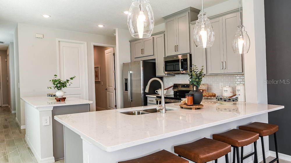 A modern kitchen features gray cabinets, white quartz countertops, and a large island with seating — 32488 SEA LOCH LOOP, MOUNT DORA, FL