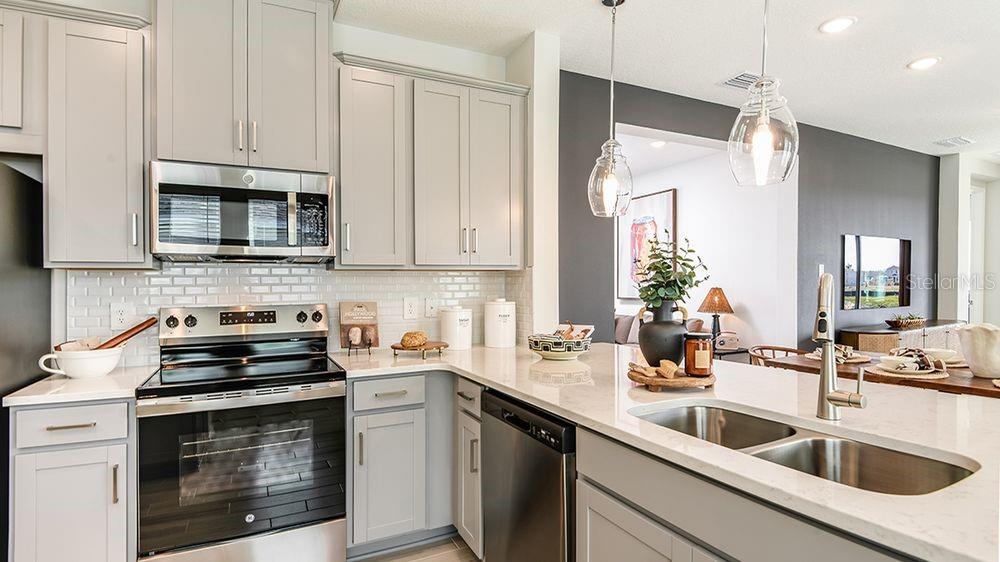 A modern kitchen features light gray cabinets, stainless steel appliances, and a white quartz island — 32488 SEA LOCH LOOP, MOUNT DORA, FL