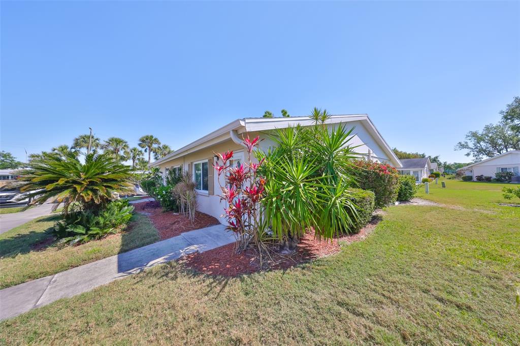 A single-story house exterior features a concrete walkway, tropical landscaping, and a grassy yard — 2202 CLUBHOUSE DRIVE UNIT 174, SUN CITY CENTER, FL