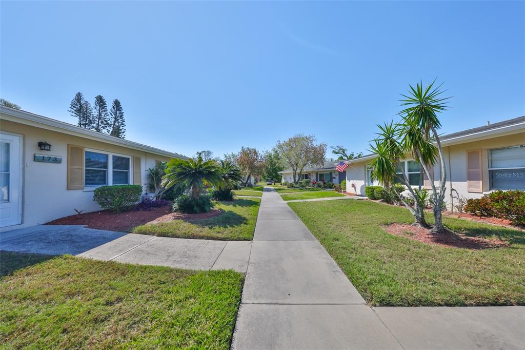 A sidewalk leads between two single-story residential buildings with lawns and landscaping — 2202 CLUBHOUSE DRIVE UNIT 174, SUN CITY CENTER, FL
