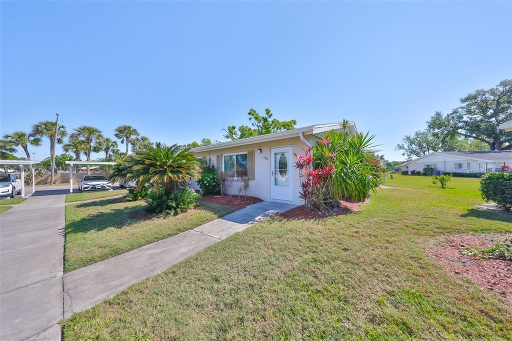 A single-story house with a white door, light-colored siding, and landscaping under a clear sky — 2202 CLUBHOUSE DRIVE UNIT 174, SUN CITY CENTER, FL